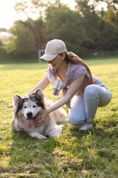Photo of Smiling woman with her cute Alaskan malamute dog on green grass outdoors in morning