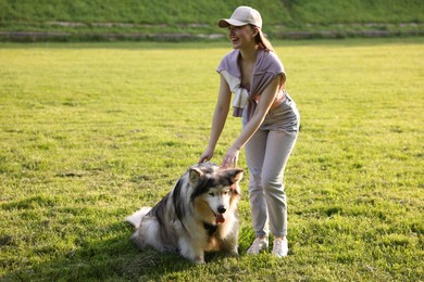 Photo of Smiling woman with her cute Alaskan malamute dog on green grass outdoors in morning
