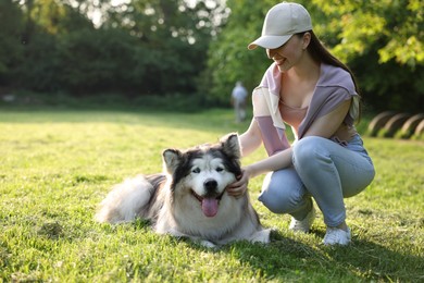 Photo of Smiling woman with her cute Alaskan malamute dog on green grass outdoors in morning