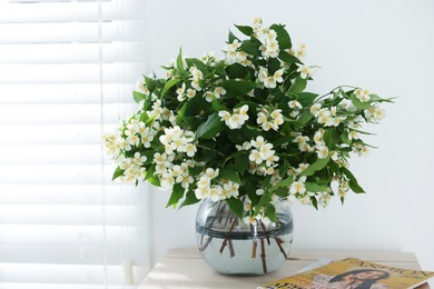 Photo of Beautiful jasmine flowers in vase on table near window indoors