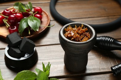 Photo of Hookah bowl with tobacco, hose, charcoal cubes, cherries and mint on wooden table, closeup