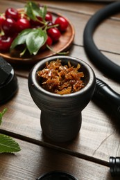 Photo of Hookah bowl with tobacco, hose and cherries on wooden table, closeup