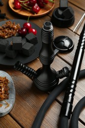 Photo of Traditional hookah parts, tobacco, charcoal cubes and cherries on wooden table, closeup