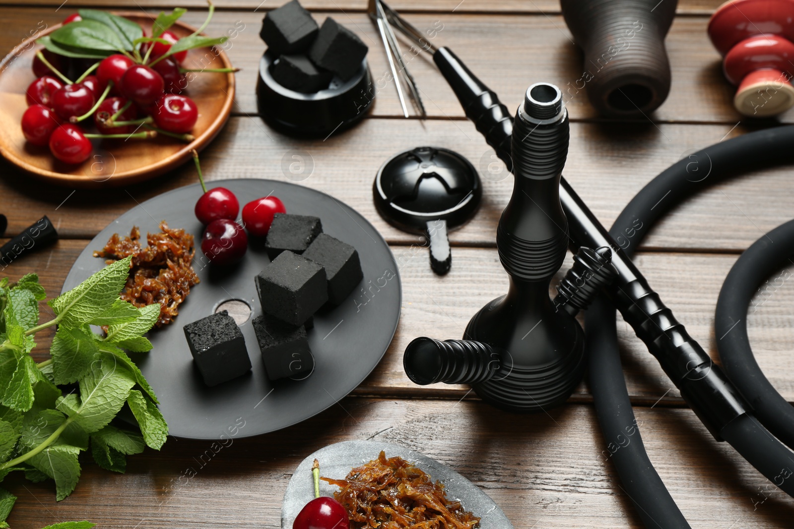 Photo of Traditional hookah parts, tobacco, charcoal cubes, cherries and mint on wooden table