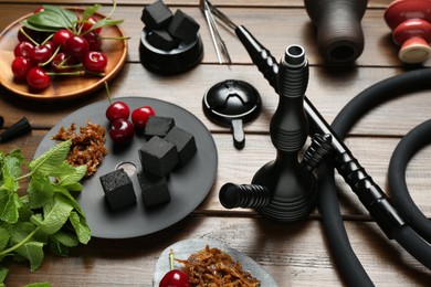 Photo of Traditional hookah parts, tobacco, charcoal cubes, cherries and mint on wooden table