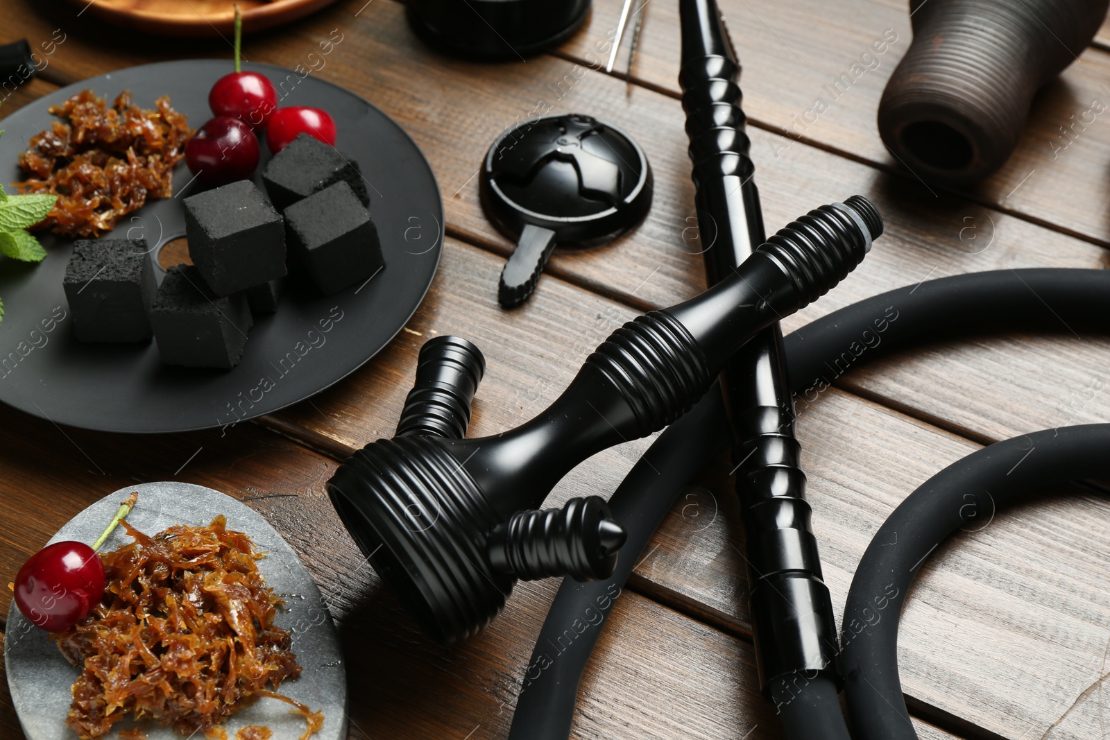 Photo of Traditional hookah parts, tobacco, charcoal cubes and cherries on wooden table