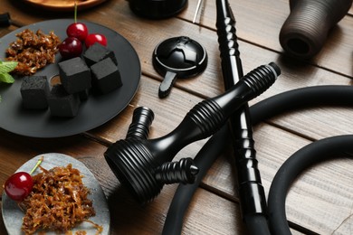Photo of Traditional hookah parts, tobacco, charcoal cubes and cherries on wooden table