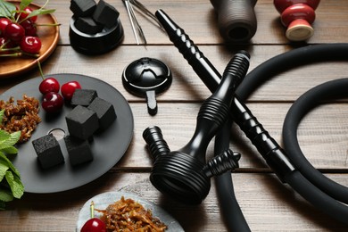 Photo of Traditional hookah parts, tobacco, charcoal cubes, cherries and mint on wooden table