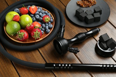 Photo of Traditional hookah parts, charcoal cubes, tobacco limes and berries on wooden table
