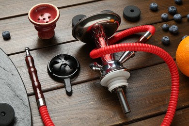 Photo of Traditional hookah parts, charcoal rings and blueberries on wooden table