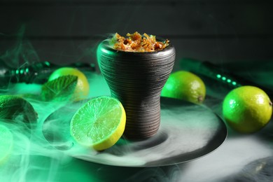 Photo of Hookah bowl with limes, mint and smoke on black table, closeup