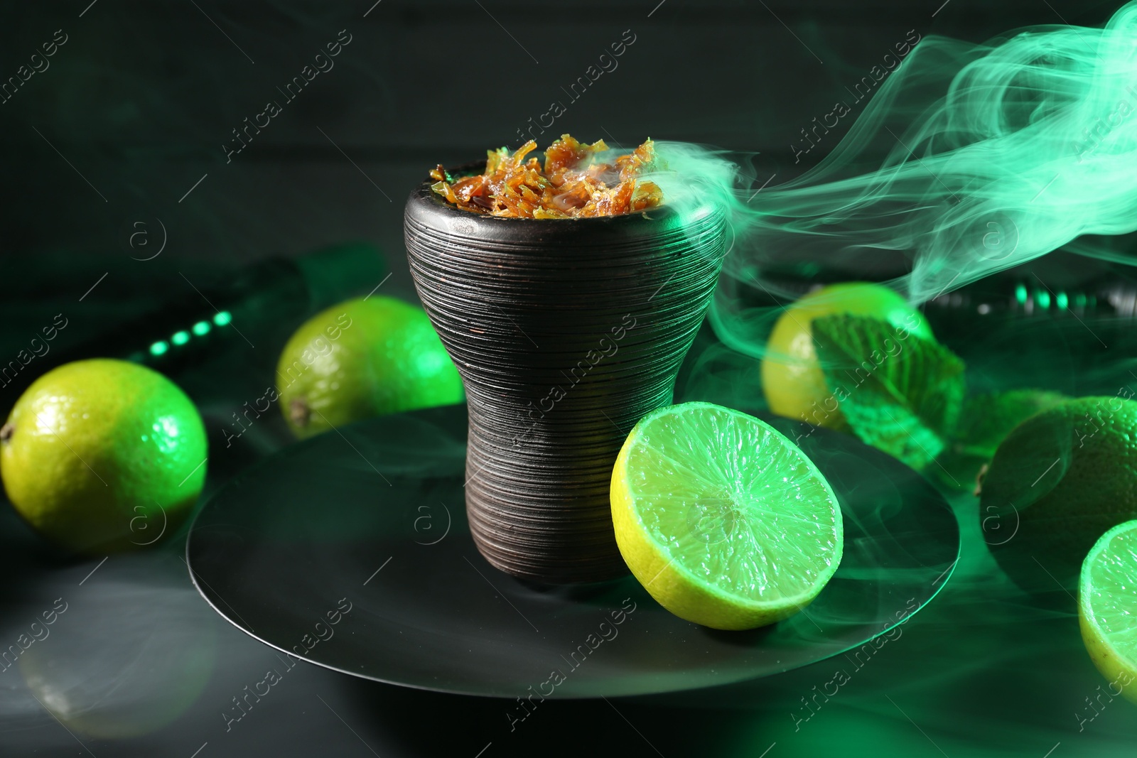 Photo of Hookah bowl with limes, mint and smoke on black table, closeup