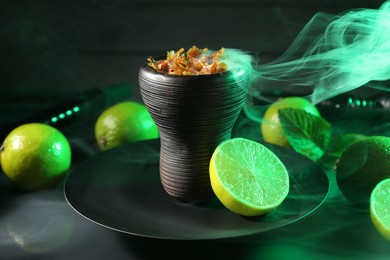 Photo of Hookah bowl with limes, mint and smoke on black table, closeup