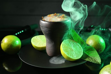 Photo of Hookah bowl with limes, mint and smoke on black table, closeup