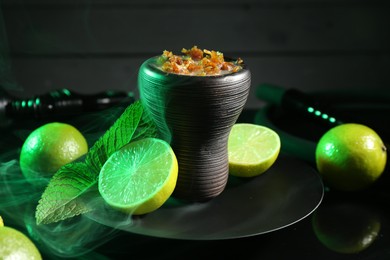 Photo of Hookah bowl with limes, mint and smoke on black table, closeup