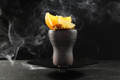 Photo of Hookah bowl with citrus fruits and smoke on black table, closeup