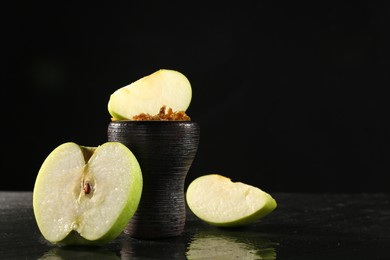 Photo of Hookah bowl with apple pieces and smoke on black table, closeup. Space for text