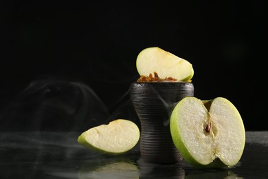 Photo of Hookah bowl with apple pieces and smoke on black table, closeup. Space for text