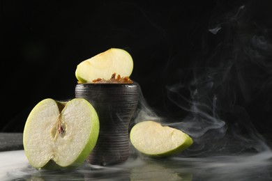 Photo of Hookah bowl with apple pieces and smoke on black table, closeup. Space for text