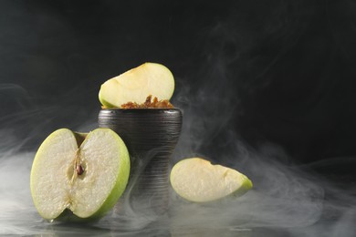 Photo of Hookah bowl with apple pieces and smoke on black table, closeup. Space for text