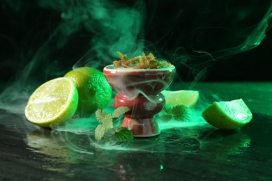 Photo of Hookah bowl with limes, mint and smoke on black table, closeup