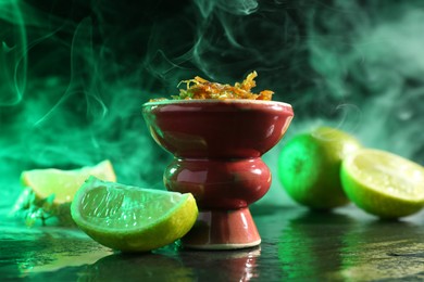 Photo of Hookah bowl with limes, mint and smoke on black table, closeup