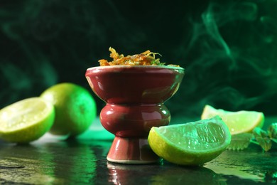 Photo of Hookah bowl with limes, mint and smoke on black table, closeup