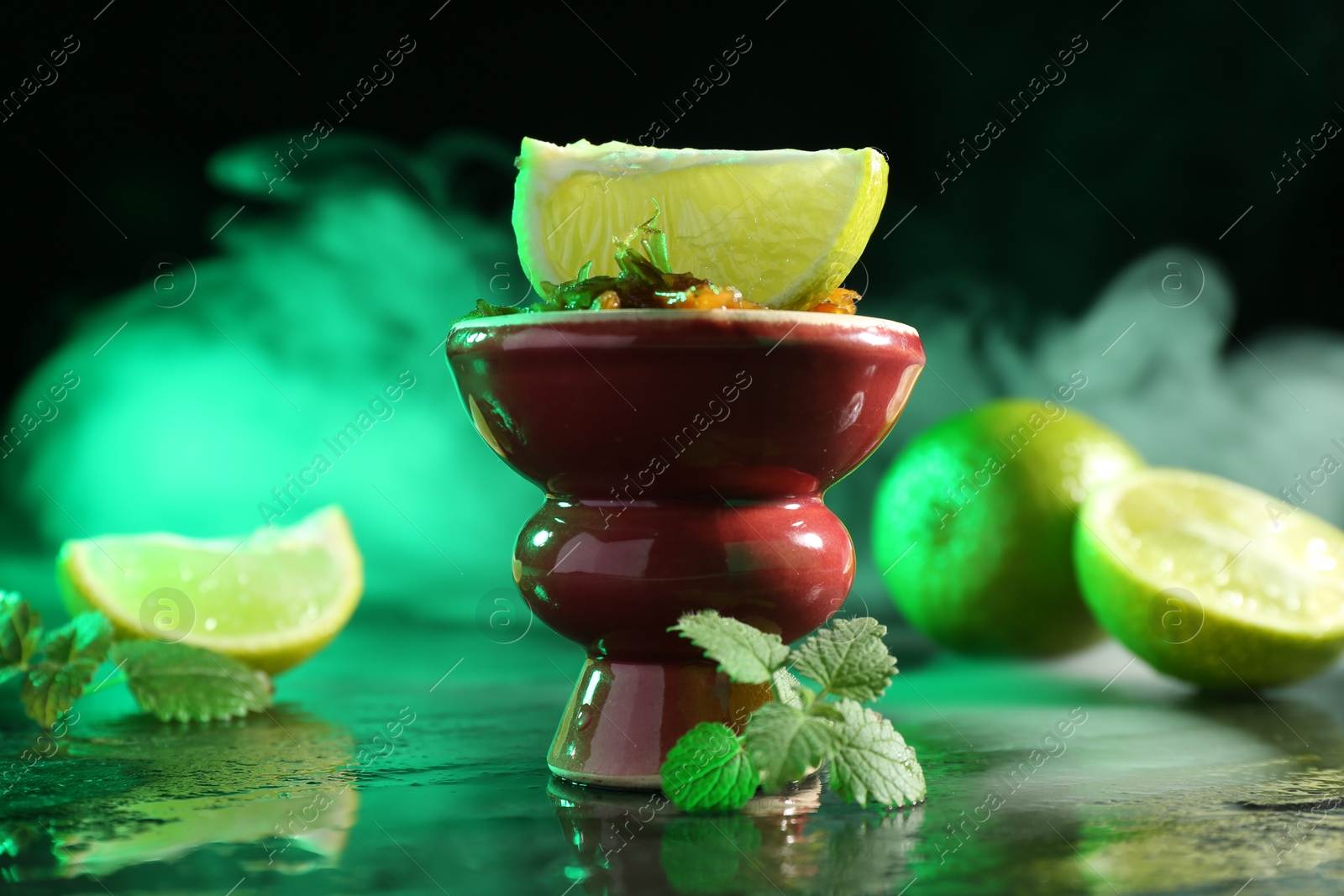 Photo of Hookah bowl with limes, mint and smoke on black table, closeup