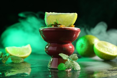 Photo of Hookah bowl with limes, mint and smoke on black table, closeup
