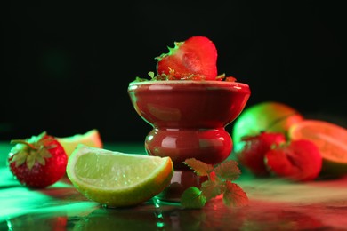 Photo of Hookah bowl with limes, strawberries, mint and smoke on black table, closeup