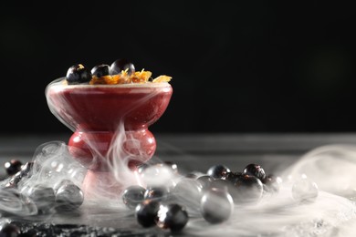 Photo of Hookah bowl with currants and smoke on black table, closeup. Space for text