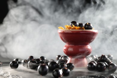 Photo of Hookah bowl with currants and smoke on black table, closeup