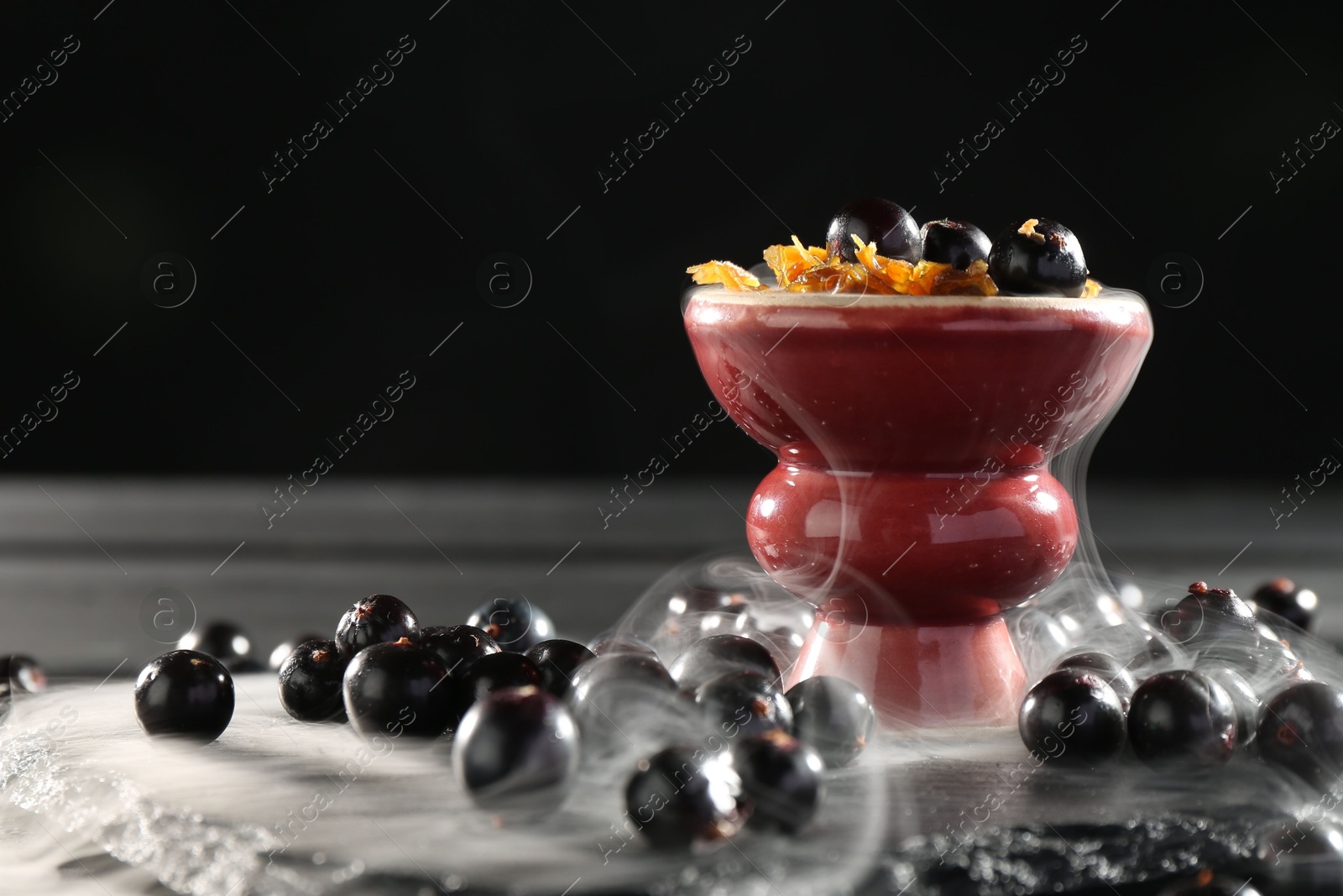 Photo of Hookah bowl with currants and smoke on black table, closeup. Space for text