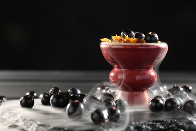 Photo of Hookah bowl with currants and smoke on black table, closeup. Space for text