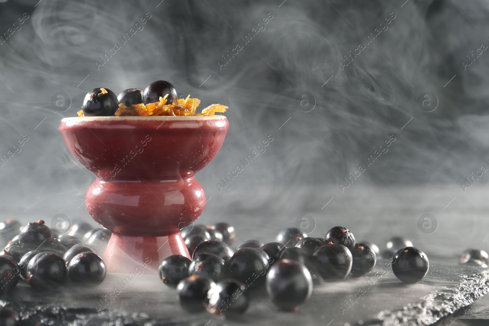 Photo of Hookah bowl with currants and smoke on black table, closeup