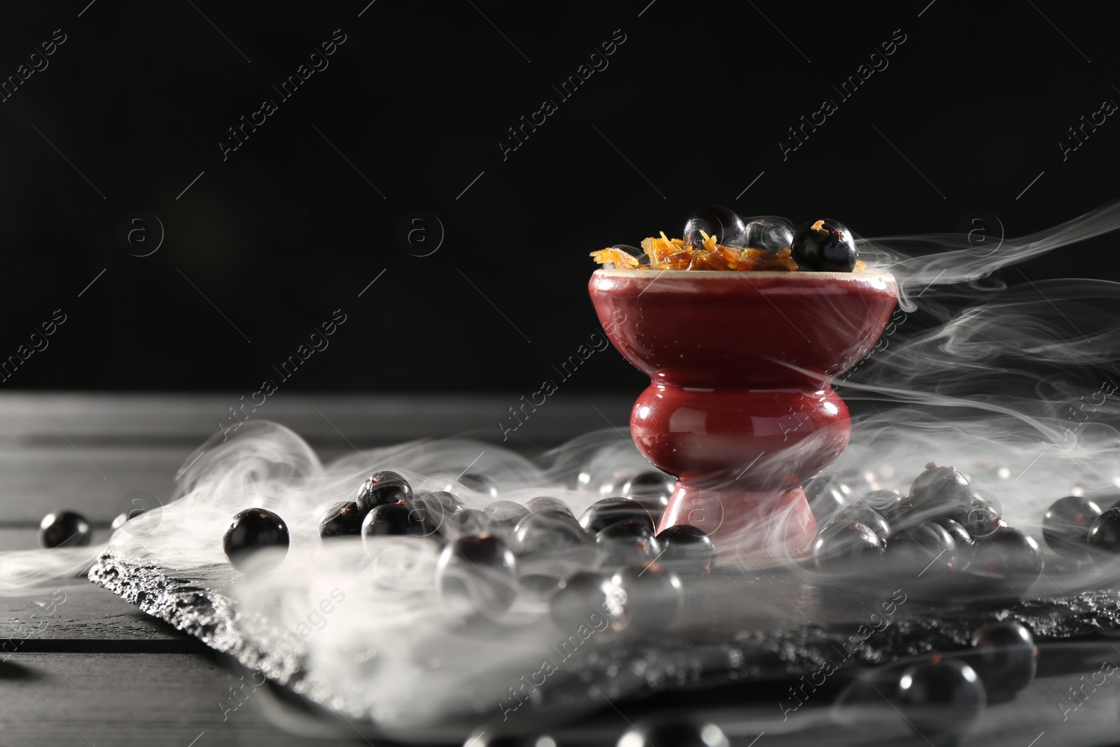 Photo of Hookah bowl with currants and smoke on black table, closeup. Space for text