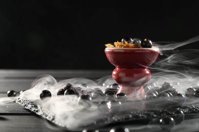 Photo of Hookah bowl with currants and smoke on black table, closeup. Space for text
