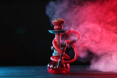 Photo of Hookah on wooden table with smoke in color lights against black background