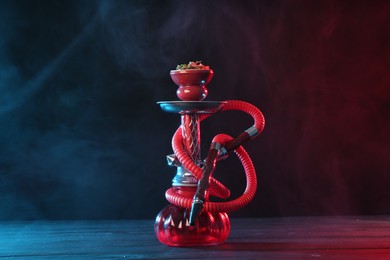 Photo of Hookah on wooden table with smoke in color lights against black background