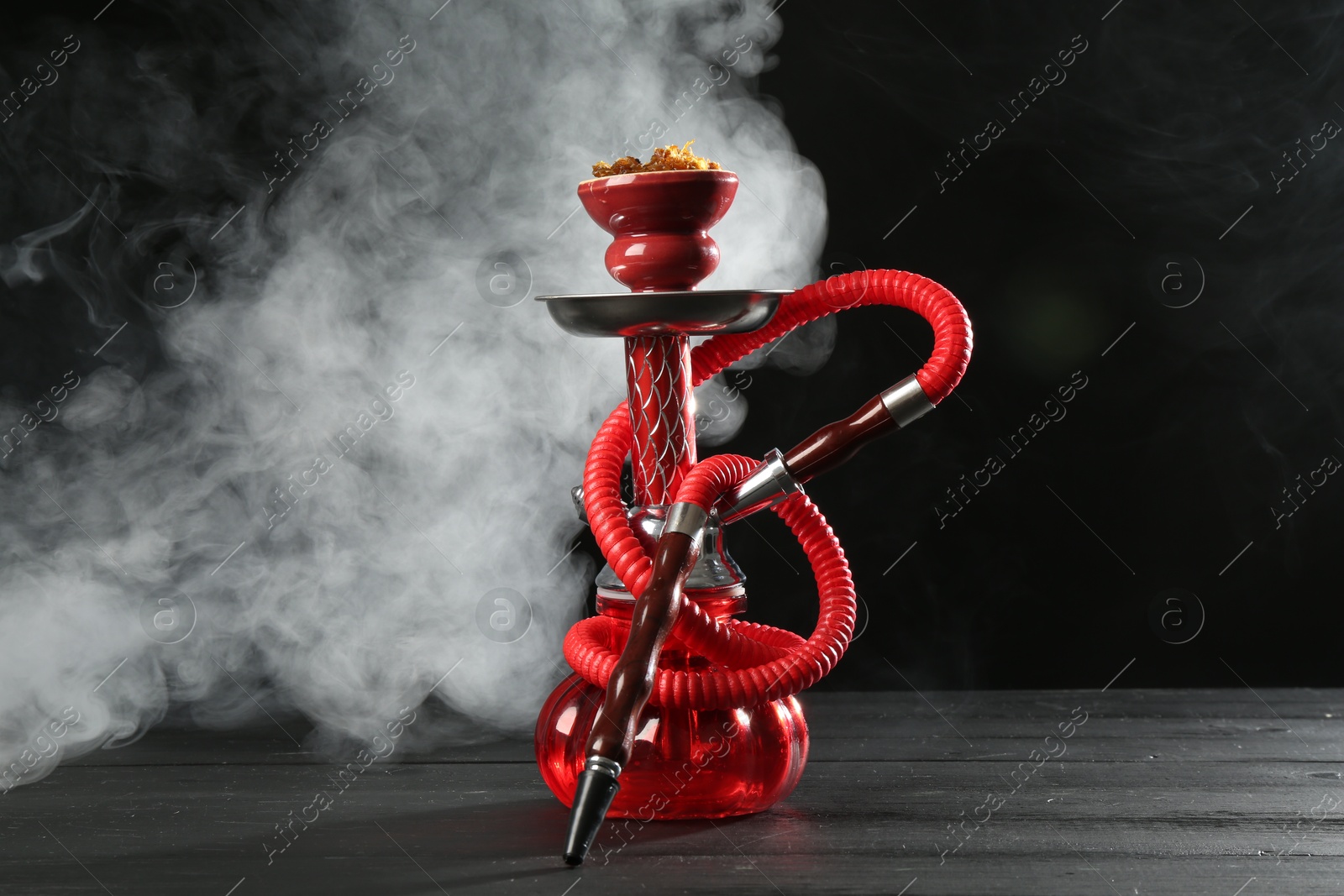 Photo of Hookah on wooden table with smoke against black background