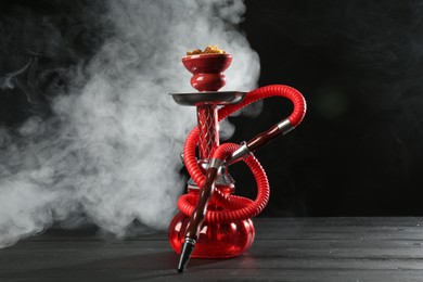 Photo of Hookah on wooden table with smoke against black background