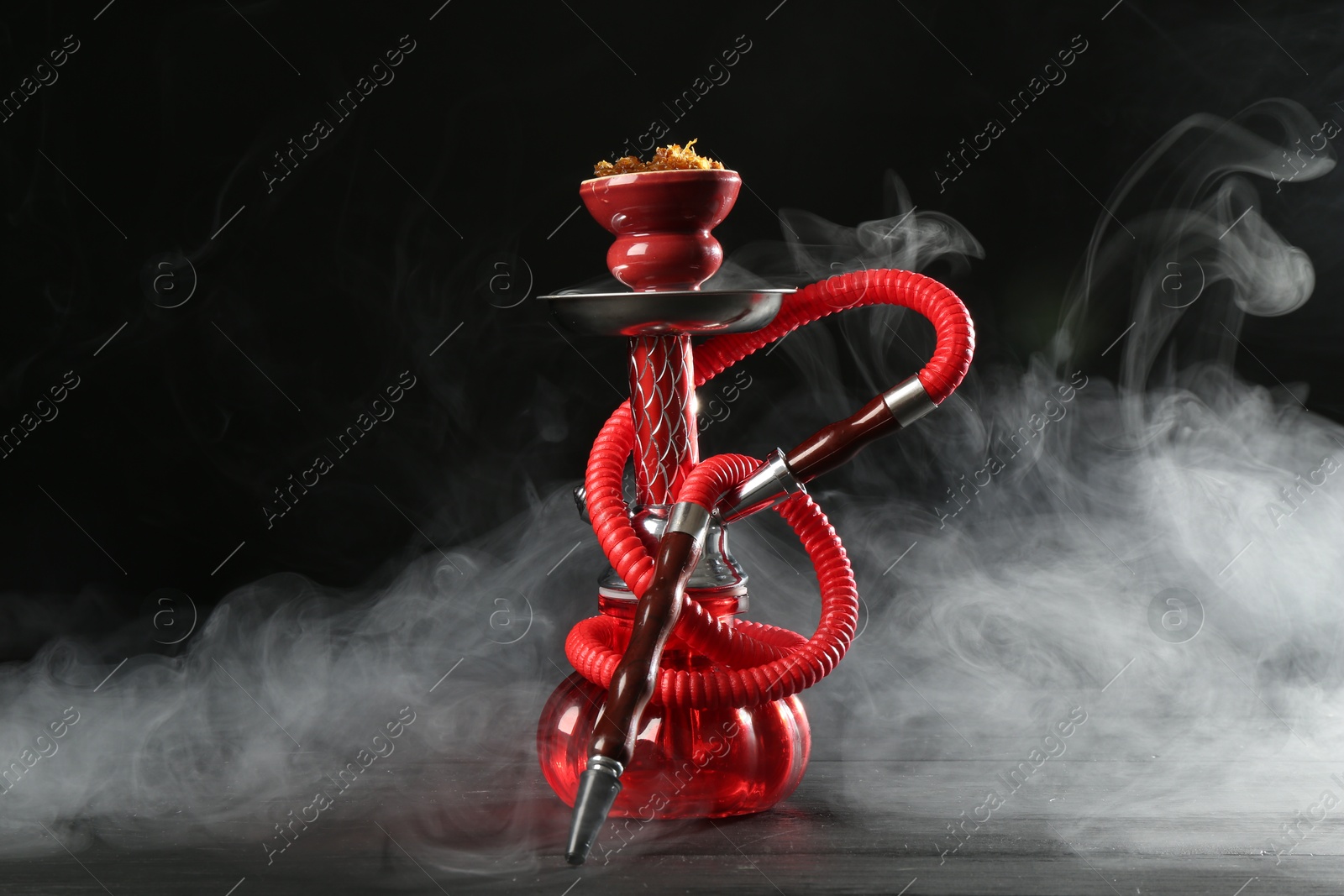 Hookah on wooden table with smoke against black background Photo of Hookah on wooden table with smoke against black background
