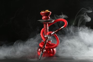 Photo of Hookah on wooden table with smoke against black background