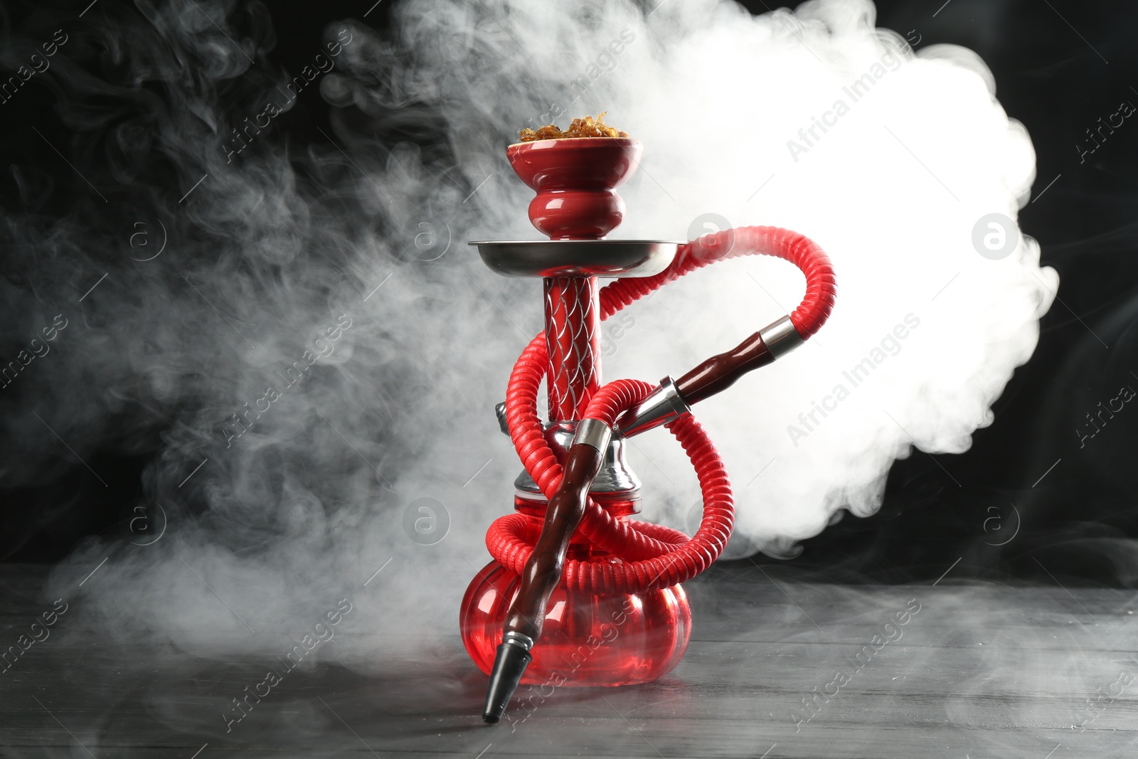 Photo of Hookah on wooden table with smoke against black background