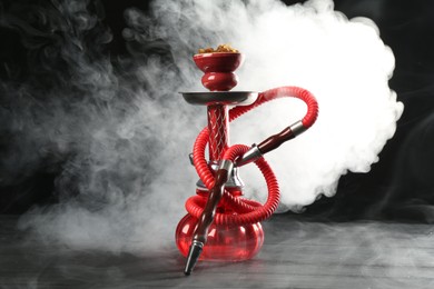 Photo of Hookah on wooden table with smoke against black background