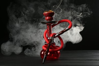Photo of Hookah on wooden table with smoke against black background