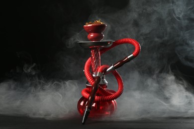 Photo of Hookah on wooden table with smoke against black background