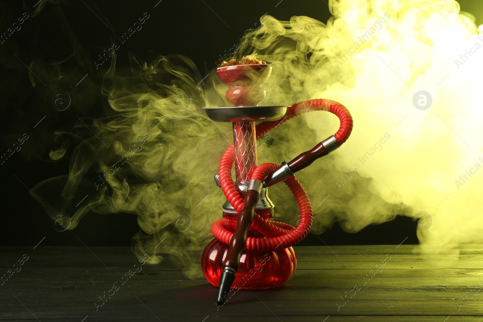 Photo of Hookah on wooden table with smoke in color lights against black background