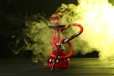 Photo of Hookah on wooden table with smoke in color lights against black background