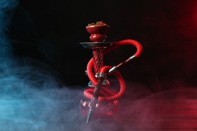 Photo of Hookah on wooden table with smoke in color lights against black background
